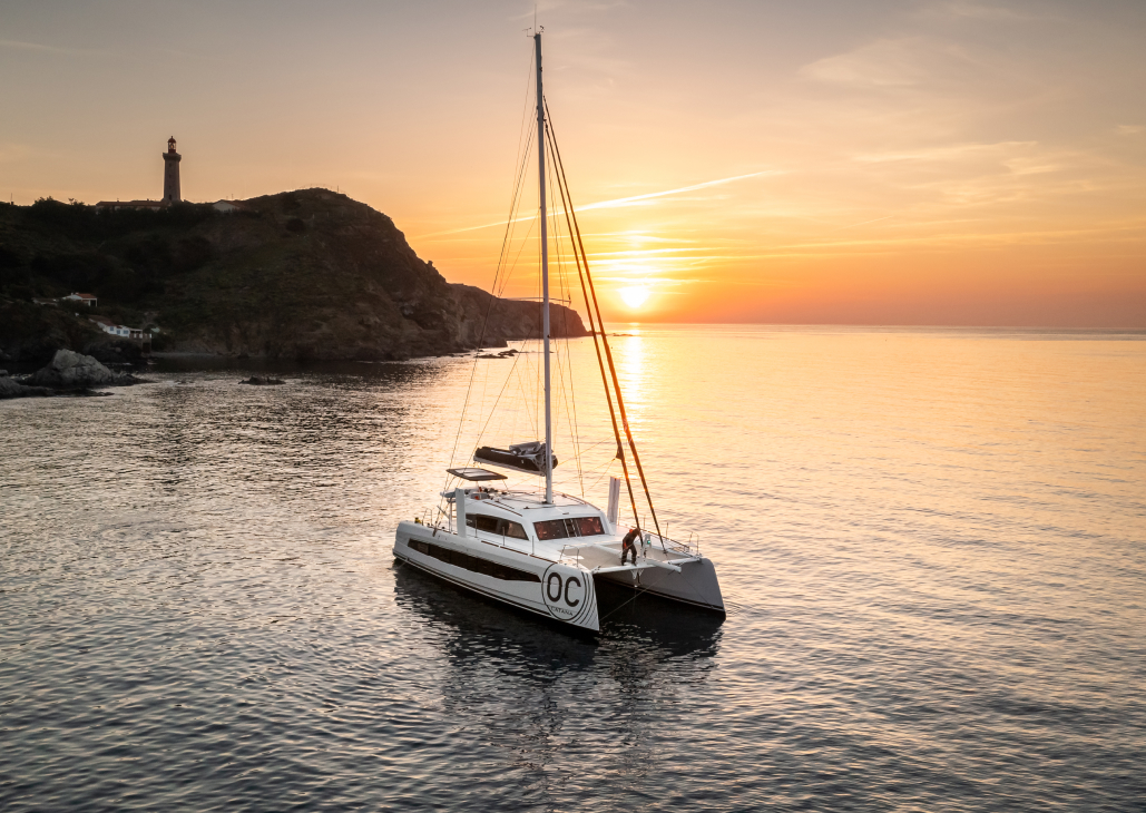Catamaran face au coucher de soleil avec la côte